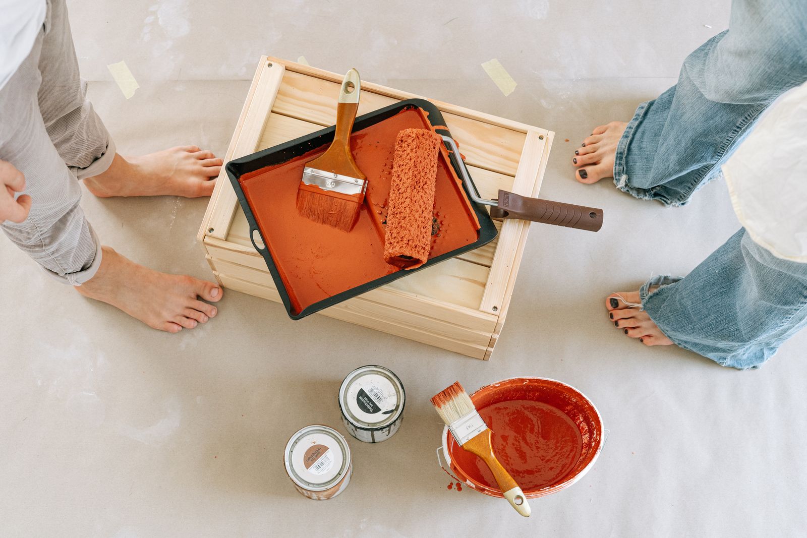 Overhead view of a renovation setup with paint, brushes, and bare feet.